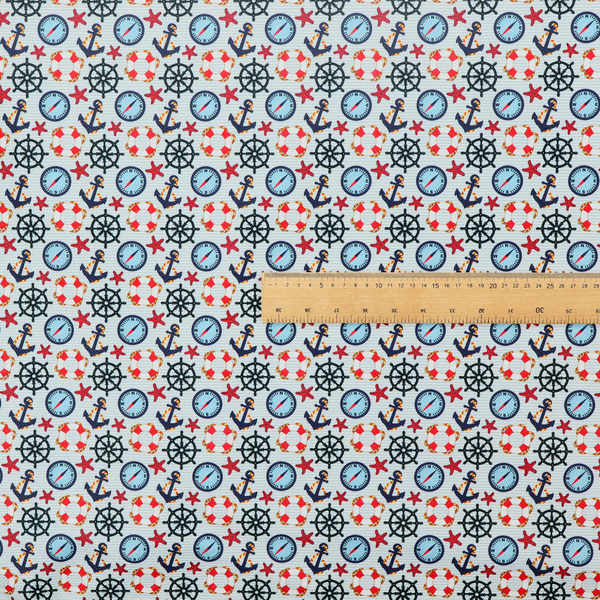 Light blue fabric with a dense repeating nautical pattern featuring dark blue anchors, black ship wheels, blue compasses, red-and-white lifebuoys, and tiny red stars.
