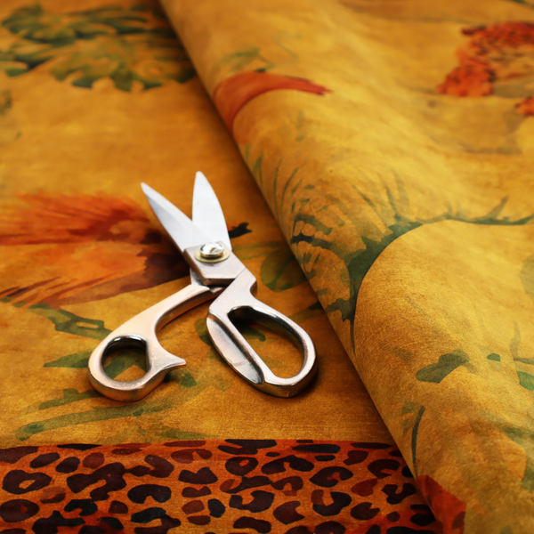 Fabric pattern featuring a warm orange and gold background with jungle wildlife, including leopards, tropical birds, large green leaves, and rocky terrain.