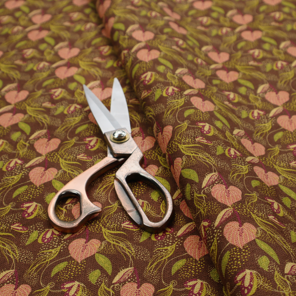 A brown upholstery fabric featuring a repeating pattern of pink heart-shaped leaves, green foliage, and delicate botanical details.