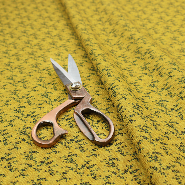 Mustard yellow fabric featuring a dense, repeating pattern of small dark green or black trailing vines with tiny leaves and a subtle woven texture.