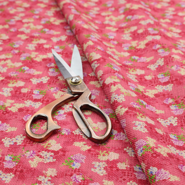 A vibrant raspberry pink fabric featuring a dense, repeating pattern of small white, purple, and green floral clusters over a subtle checked texture.