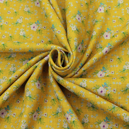 Textured mustard yellow fabric featuring a repeating micro floral pattern of small white and pink blossoms with green leaves and blue accents.