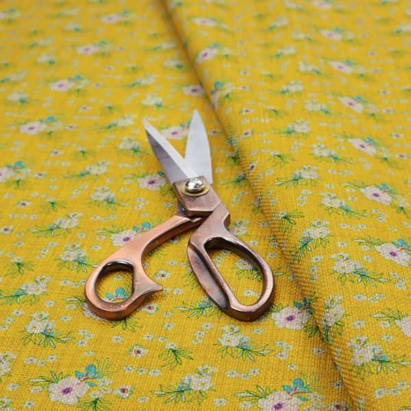 Textured mustard yellow fabric featuring a repeating micro floral pattern of small white and pink blossoms with green leaves and blue accents.
