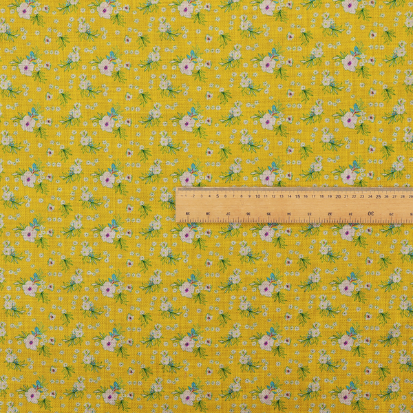 Textured mustard yellow fabric featuring a repeating micro floral pattern of small white and pink blossoms with green leaves and blue accents.
