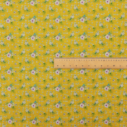Textured mustard yellow fabric featuring a repeating micro floral pattern of small white and pink blossoms with green leaves and blue accents.