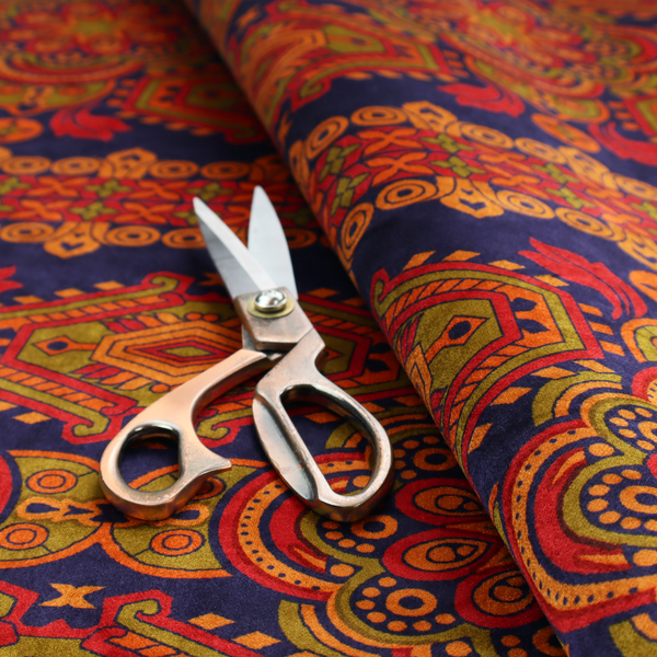 A deep purple textile adorned with intricate, ornate patterns including large mandala medallions, geometric motifs, and a central horizontal decorative stripe in shades of red, orange, and olive green.