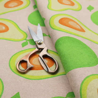 A repeating pattern fabric featuring whimsical illustrations of whole green avocados with small leaves and sliced avocado halves showing bright orange pits, all scattered across a light pink background.