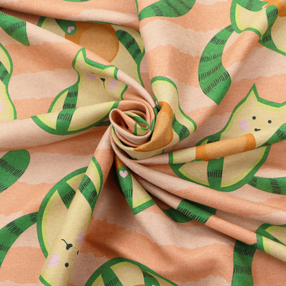 A playful repeating pattern fabric featuring whimsical illustrated "avocatos"—cats shaped like avocado halves with green striped tails and orange pits—over a light peach background with horizontal orange stripes.