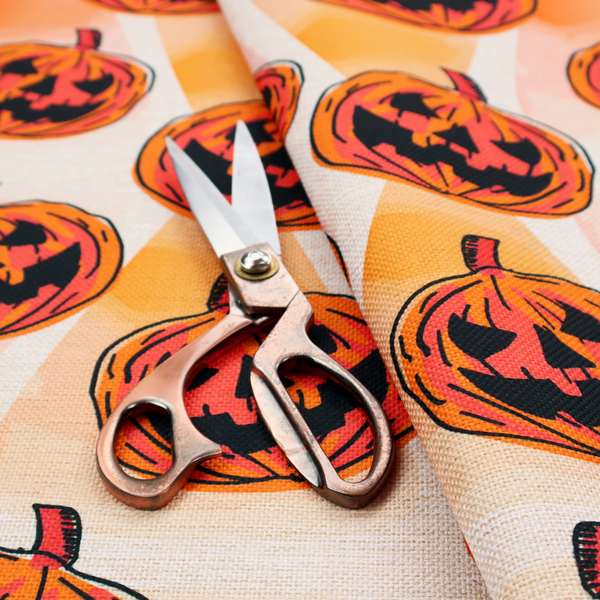 A seamless, repeating Halloween-themed pattern featuring vibrant orange carved jack-o'-lantern pumpkins with bold, black spooky expressions and lined details set against an abstract geometric orange and cream background.