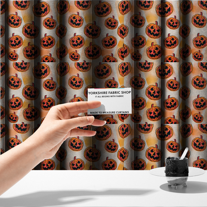 The fabric used to create these made-to-measure curtains is a seamless, repeating Halloween-themed pattern featuring vibrant orange carved jack-o'-lantern pumpkins with bold, black spooky expressions and lined details set against an abstract geometric orange and cream background.