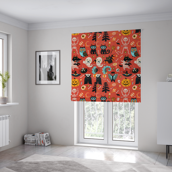 The fabric used to create these Roman blinds is a seamless, repeating Halloween-themed pattern featuring a vibrant red-orange background filled with a dancing skeleton, vampires, a mummified dog, a blue owl, black cats, a flying bat, ghosts, a jack-o'-lantern, candy, skulls, trees, and whimsical monsters.