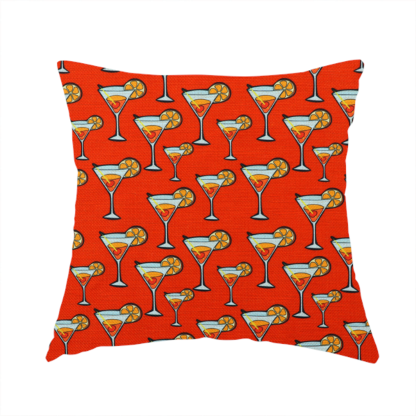 The fabric used to create this handmade cushion is a repeating pattern of cocktail glasses filled with orange liquid, garnished with a slice of orange and a cherry, set against a bright red background.