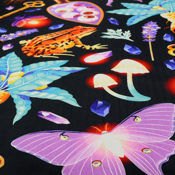 A vibrant, repeating mystical pattern on a black background featuring illustrated mandrake roots with faces, orange frogs, purple moths, glowing fireflies, potion bottles filled with eyeballs, ornate golden keys, luminescent mushrooms, lavender sprigs, and scattered crystals.