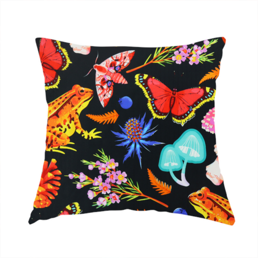 The fabric used to create this handmade cushion is a vibrant, repeating botanical pattern on a black background featuring bright red butterflies, orange spotted frogs, orange pinecones, pink and white mushrooms, orange fern fronds, blue berries, and purple wildflowers.