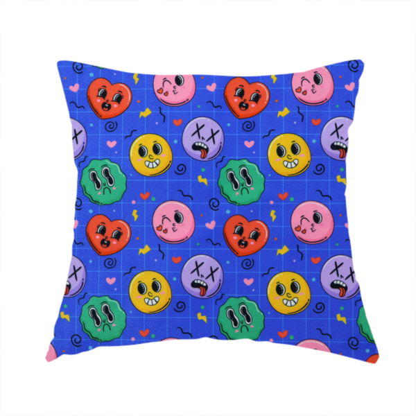 The fabric used to create this handmade cushion is a repeating pattern of quirky cartoon characters, including winking faces, hearts, green blobs, and dizzy expressions with X eyes, scattered over a blue grid background.