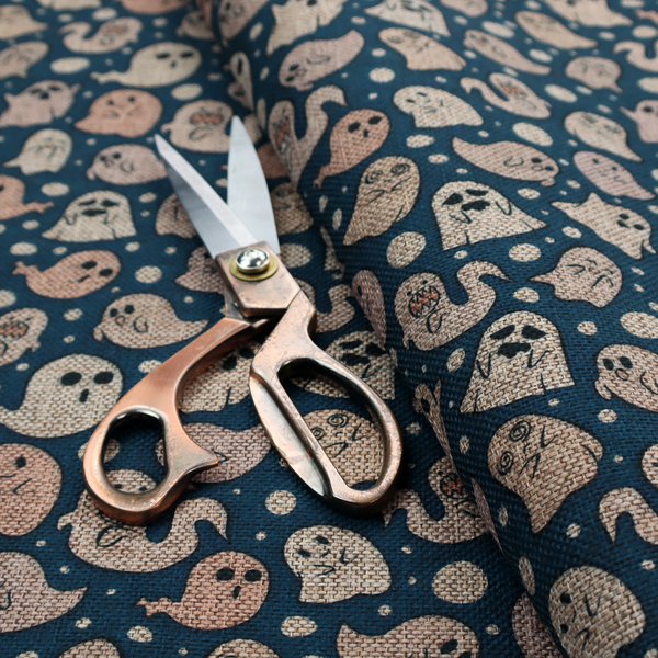 A dark blue fabric patterned with an all-over, repeating design of light beige and peach cartoon ghosts with various cute and silly facial expressions, interspersed with small white polka dots.