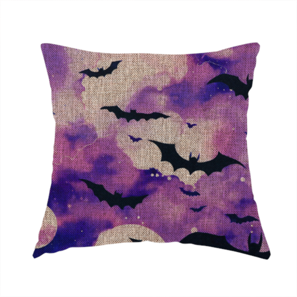 The fabric used to create this handmade cushion is a watercolour-style Halloween fabric featuring a spooky night sky in shades of purple and pink, filled with silhouettes of flying black bats and two pale full moons.