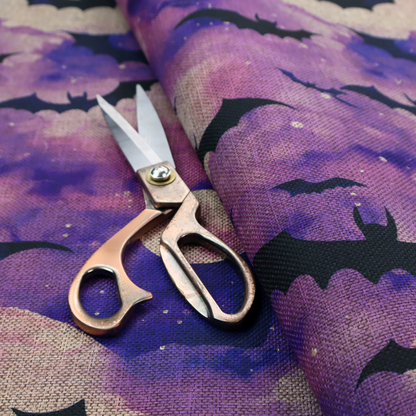 A watercolour-style Halloween fabric featuring a spooky night sky in shades of purple and pink, filled with silhouettes of flying black bats and two pale full moons.