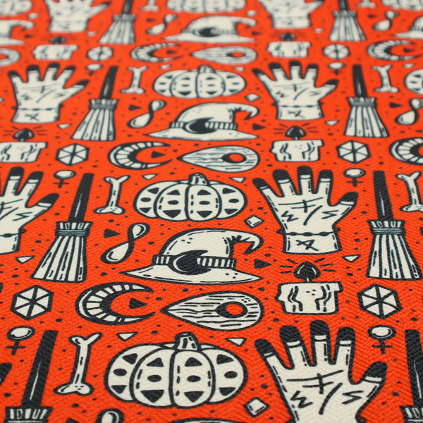 An orange Halloween fabric patterned with repeating black and white illustrations of patterned pumpkins, mystical hands with symbols, witch hats with crescent moons, brooms, candles, bones, and planchettes.