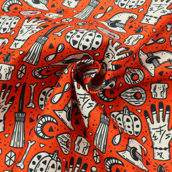 An orange Halloween fabric patterned with repeating black and white illustrations of patterned pumpkins, mystical hands with symbols, witch hats with crescent moons, brooms, candles, bones, and planchettes.