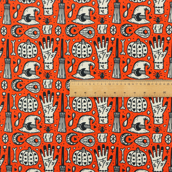 An orange Halloween fabric patterned with repeating black and white illustrations of patterned pumpkins, mystical hands with symbols, witch hats with crescent moons, brooms, candles, bones, and planchettes.