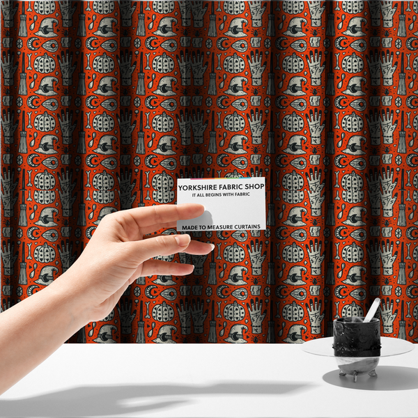 The fabric used to create these made-to-measure curtains is an orange Halloween fabric patterned with repeating black and white illustrations of patterned pumpkins, mystical hands with symbols, witch hats with crescent moons, brooms, candles, bones, and planchettes.