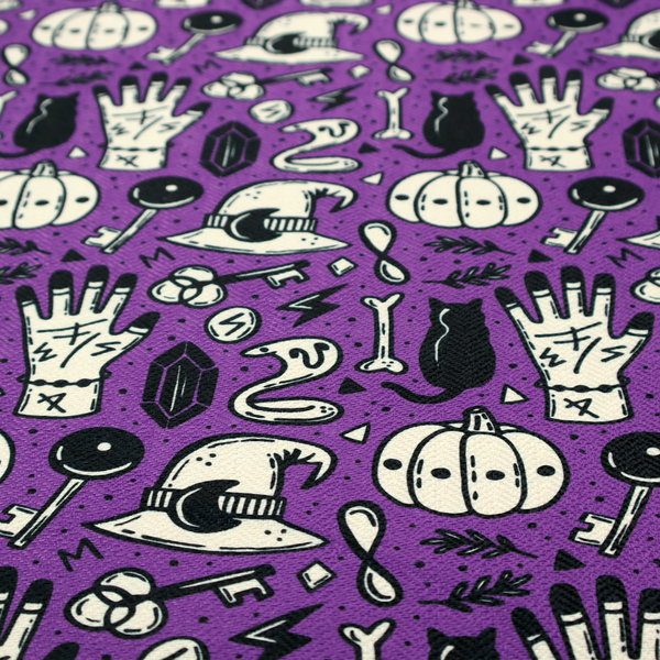 A purple Halloween fabric patterned with repeating black and cream illustrations of pumpkins, witch hats, black cats, mystical marked hands, snakes, keys, bones, and crystals.