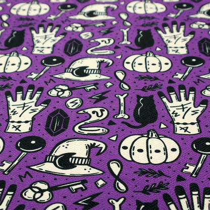 A purple Halloween fabric patterned with repeating black and cream illustrations of pumpkins, witch hats, black cats, mystical marked hands, snakes, keys, bones, and crystals.