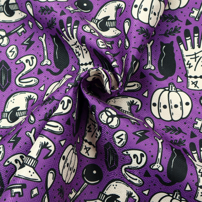 A purple Halloween fabric patterned with repeating black and cream illustrations of pumpkins, witch hats, black cats, mystical marked hands, snakes, keys, bones, and crystals.