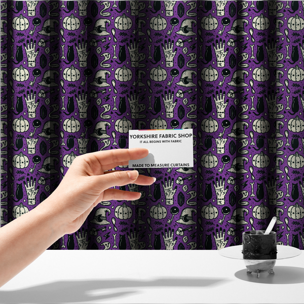 The fabric used to create these made-to-measure curtains is a purple Halloween fabric patterned with repeating black and cream illustrations of pumpkins, witch hats, black cats, mystical marked hands, snakes, keys, bones, and crystals.