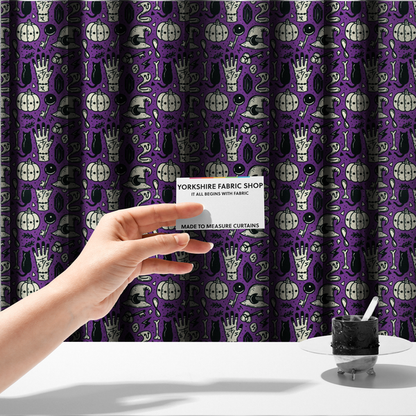 The fabric used to create these made-to-measure curtains is a purple Halloween fabric patterned with repeating black and cream illustrations of pumpkins, witch hats, black cats, mystical marked hands, snakes, keys, bones, and crystals.