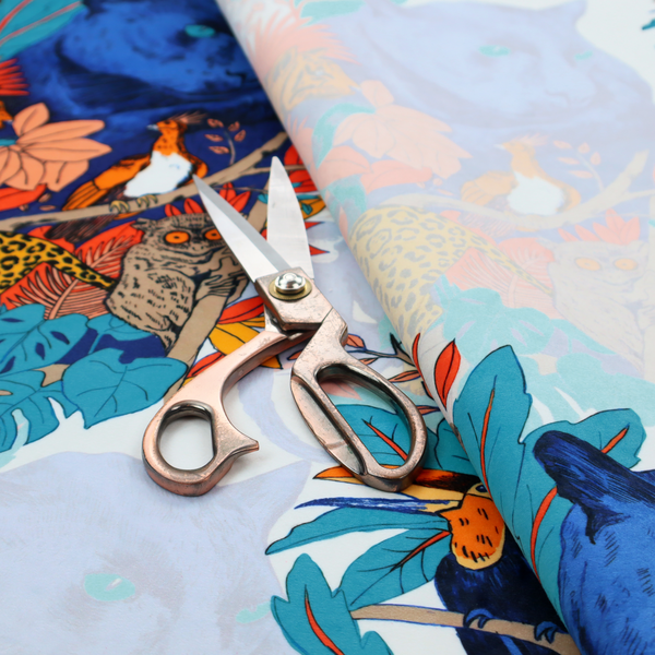 A colourful and vibrant jungle pattern on a pale background featuring a blue panther, tigers, leopards, monkeys, toucans, and lush tropical flora.