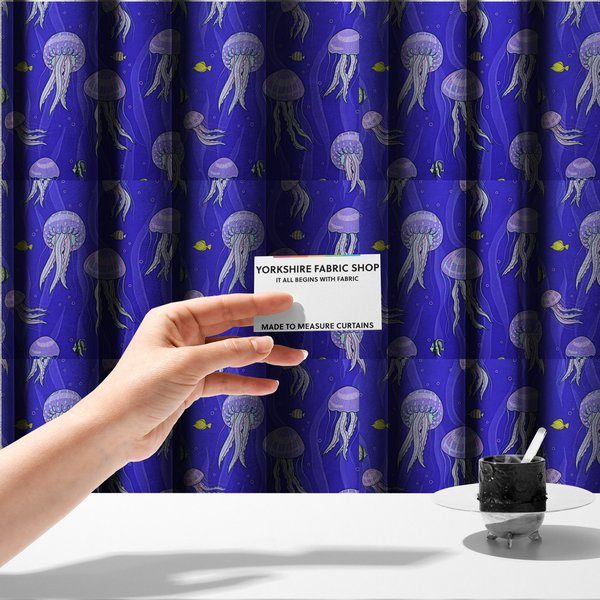 The fabric used to create these made-to-measure curtains is a vibrant underwater pattern on a rich blue background featuring glowing purple and pink jellyfish, tiny colourful fish, and floating bubbles.
