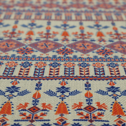 Intricate folk-inspired fabric featuring horizontal bands of geometric diamonds, stylized birds, and floral motifs in navy blue and rust orange on a beige background.