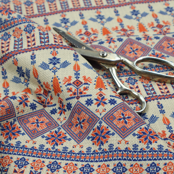 Intricate folk-inspired fabric featuring horizontal bands of geometric diamonds, stylized birds, and floral motifs in navy blue and rust orange on a beige background.