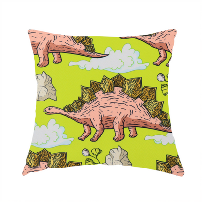 The fabric used to create this handmade cushion is a repeating pattern on a vibrant green background featuring pink Stegosaurus dinosaurs with golden plates, interspersed with light grey rocks, fluffy white clouds, and small green sprigs.
