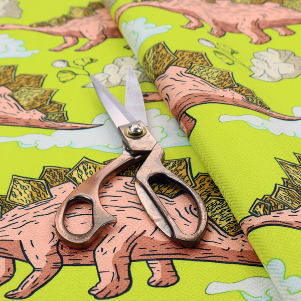 A repeating pattern on a vibrant green background featuring pink Stegosaurus dinosaurs with golden plates, interspersed with light grey rocks, fluffy white clouds, and small green sprigs.