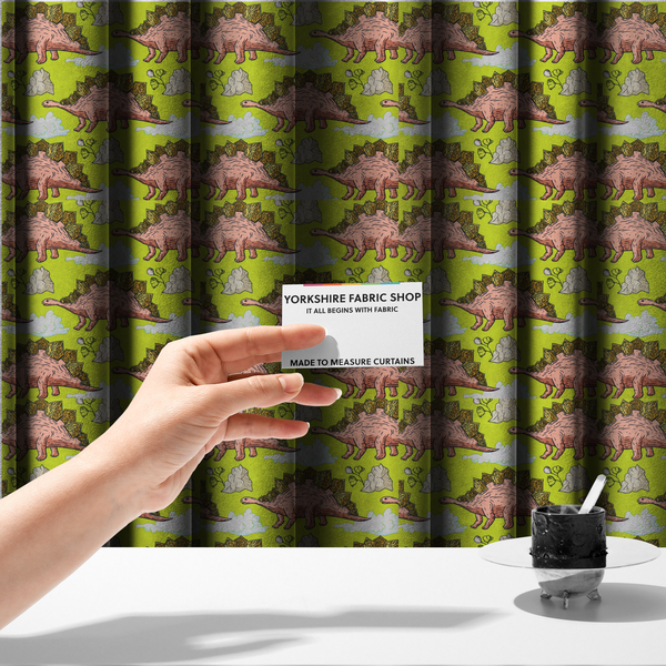 The fabric used to create these made-to-measure curtains is a repeating pattern on a vibrant green background featuring pink Stegosaurus dinosaurs with golden plates, interspersed with light grey rocks, fluffy white clouds, and small green sprigs.