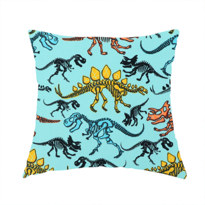 The fabric used to create this handmade cushion is a repeating pattern on a light blue background featuring colourful dinosaur skeletons in yellow, orange, blue, and black, depicting various species including Stegosaurus, Triceratops, and Tyrannosaurus rex.