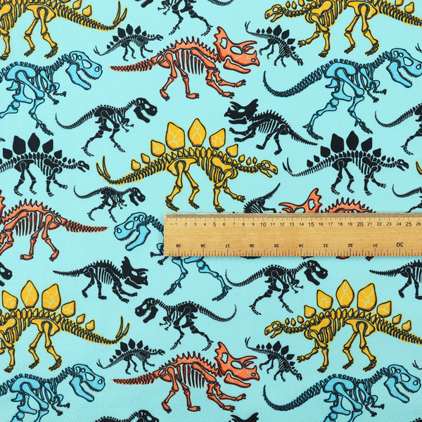 A repeating pattern on a light blue background featuring colourful dinosaur skeletons in yellow, orange, blue, and black, depicting various species including Stegosaurus, Triceratops, and Tyrannosaurus rex.