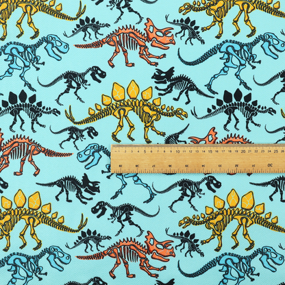 A repeating pattern on a light blue background featuring colourful dinosaur skeletons in yellow, orange, blue, and black, depicting various species including Stegosaurus, Triceratops, and Tyrannosaurus rex.