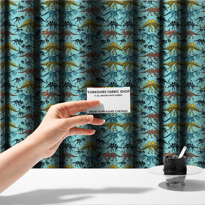 The fabric used to create these made-to-measure curtains is a repeating pattern on a light blue background featuring colourful dinosaur skeletons in yellow, orange, blue, and black, depicting various species including Stegosaurus, Triceratops, and Tyrannosaurus rex.