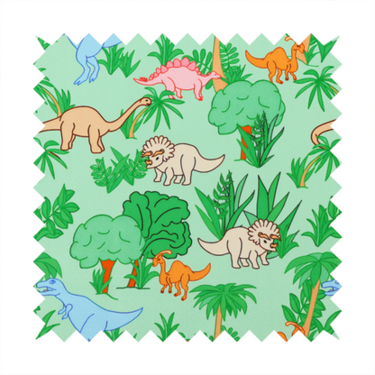 A repeating pattern on a light green background featuring colourful illustrated dinosaurs—including blue T-Rexes, pink Stegosauruses, beige Triceratopses, and orange sauropods—surrounded by green palm trees, bushes, and tropical foliage.