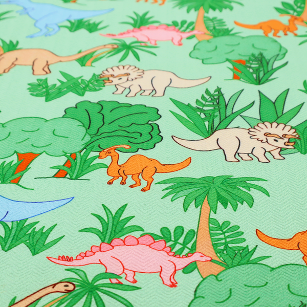 A repeating pattern on a light green background featuring colourful illustrated dinosaurs—including blue T-Rexes, pink Stegosauruses, beige Triceratopses, and orange sauropods—surrounded by green palm trees, bushes, and tropical foliage.