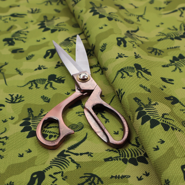 A military-style green camouflage pattern featuring repeating black dinosaur skeletons, bones, footprints, and fossils.