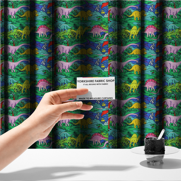 The fabric used to create these made-to-measure curtains is a vibrant, colourful repeating pattern featuring various cartoon dinosaurs including a pink long-neck, yellow triceratops, green T-Rex, and flying pterodactyls amidst a prehistoric landscape.