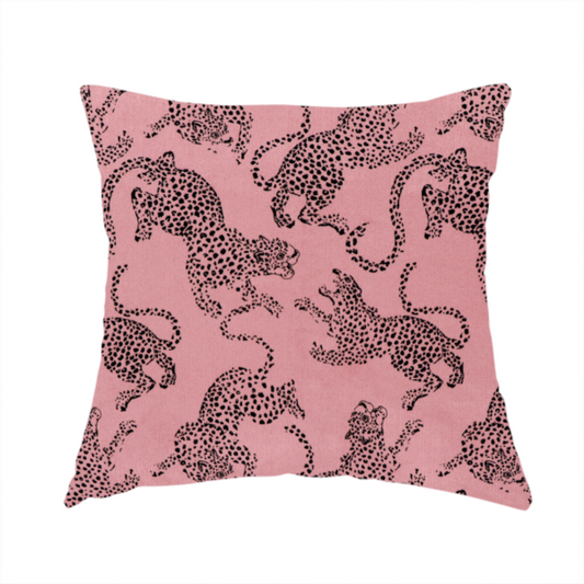 The fabric used to create this handmade cushion is a seamless repeating pattern featuring black stylized leopards or jaguars printed over a muted pink or dusty rose background. The felines are depicted in a dynamic, crouching or leaping pose with detailed spotted markings and long, curving tails.