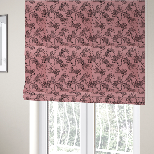 The fabric used to create these Roman blinds is a seamless repeating pattern featuring black stylized leopards or jaguars printed over a muted pink or dusty rose background. The felines are depicted in a dynamic, crouching or leaping pose with detailed spotted markings and long, curving tails.