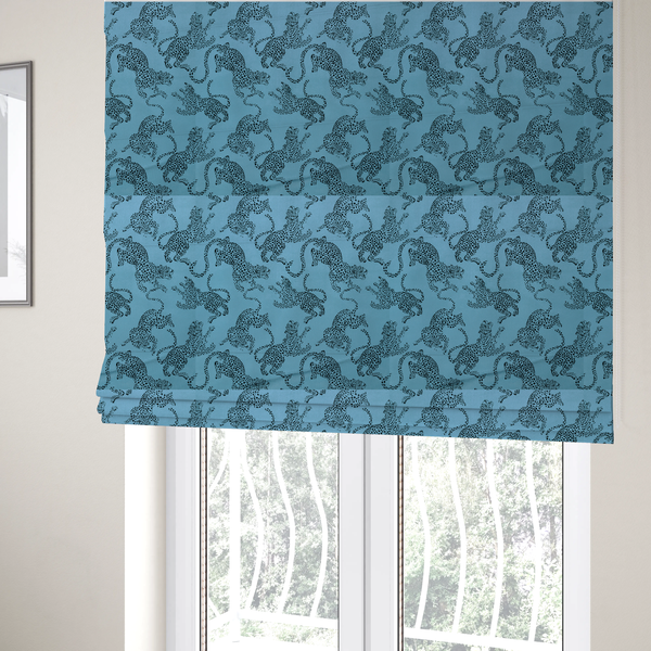 The fabric used to create these Roman blinds is a seamless repeating pattern featuring black stylized leopards or jaguars printed over a vibrant blue background. The felines are depicted in a dynamic, crouching or leaping pose with detailed spotted markings and long, curving tails.