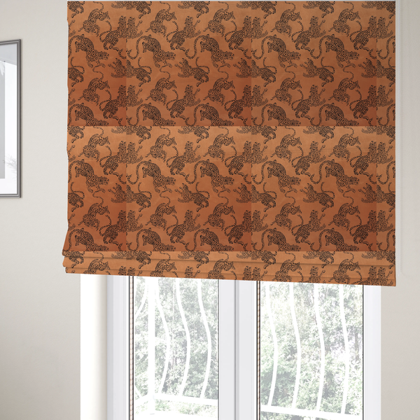 The fabric used to create these Roman blinds is a seamless repeating pattern featuring black stylized leopards or jaguars printed over a warm terracotta or burnt orange background. The felines are depicted in a dynamic, crouching or leaping pose with detailed spotted markings and long, curving tails.